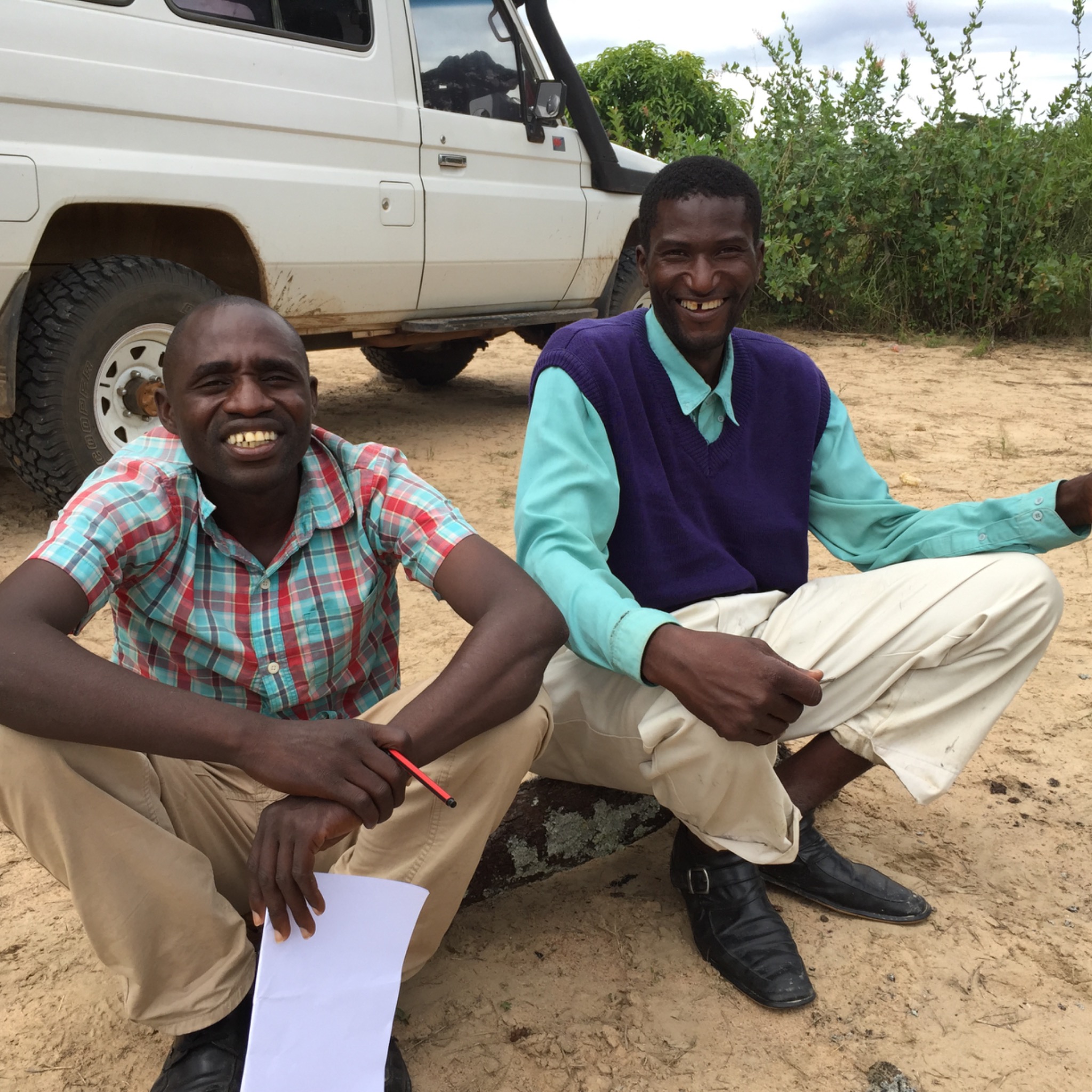 Two Zambian men smiling together beside a vehicle